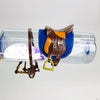 A brown horse saddle and riding prop accessory with a blue fabric backing is displayed on a clear plastic bottle.