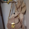A light pink quilted acrylic bag with a gold clasp and a braided chain strap hanging on a wooden rack.