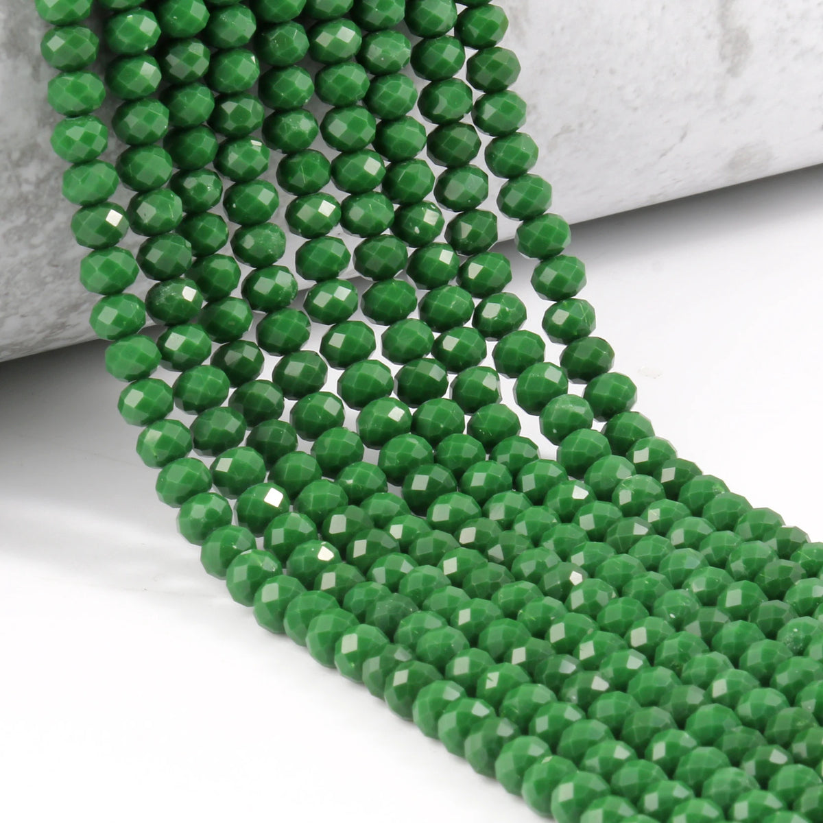 A strand of green faceted crystal glass beads laid across a white surface.