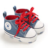 A pair of blue denim canvas baby shoes with red laces and white soles.