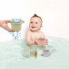 A baby is playing with a set of boat-shaped stacking cups and a larger bath toy cup in water.