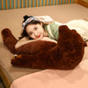 A young woman is lying down with her arms around an oversized lifelike brown bear plush cushion on a beige surface.