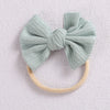 A light mint green fabric bow headband with a beige elastic band.