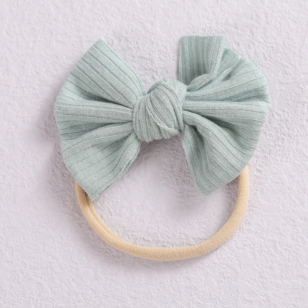 A light mint green fabric bow headband with a beige elastic band.