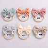 A collection of eight soft elastic hair bows in various pastel shades, including mint green, peach, pink, gray, and cream.