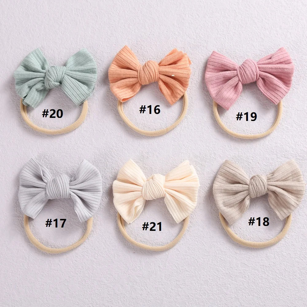 A collection of eight soft elastic hair bows in various pastel shades, including mint green, peach, pink, gray, and cream.