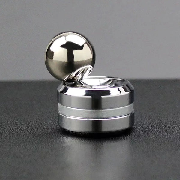 A silver metal desktop fidget spinner with a spherical top and a flat base resting on a dark surface.