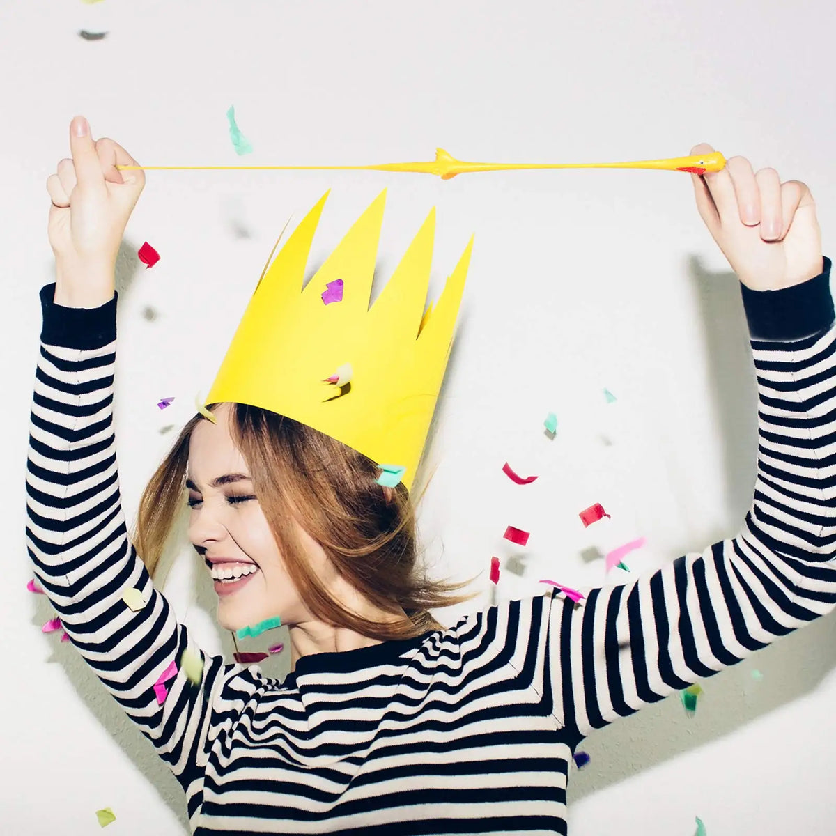 A woman holds a yellow crown with a yellow chicken toy stretched between her hands against a white background.
