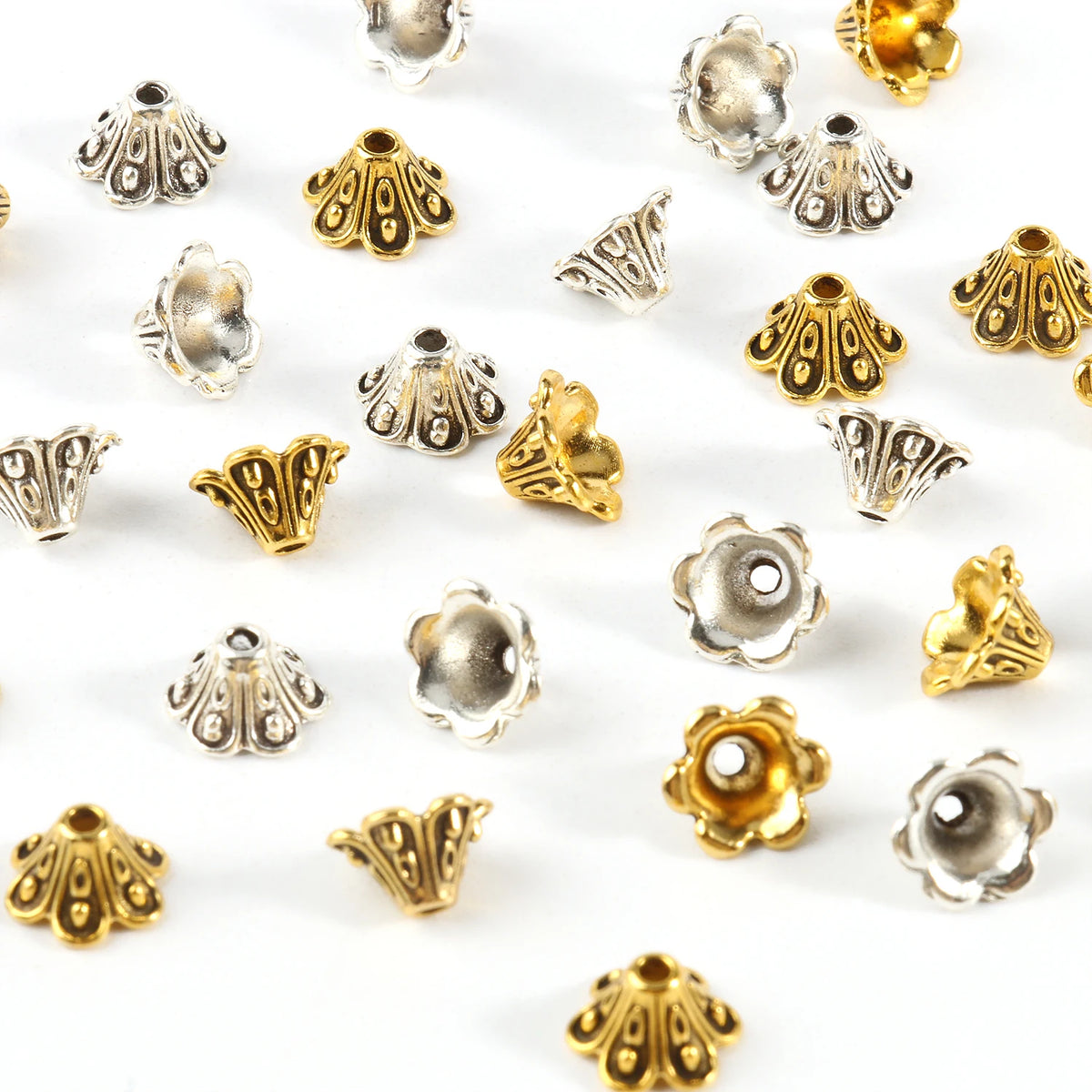 A collection of small, metallic flower-shaped bead caps in silver and gold finishes for jewelry making.