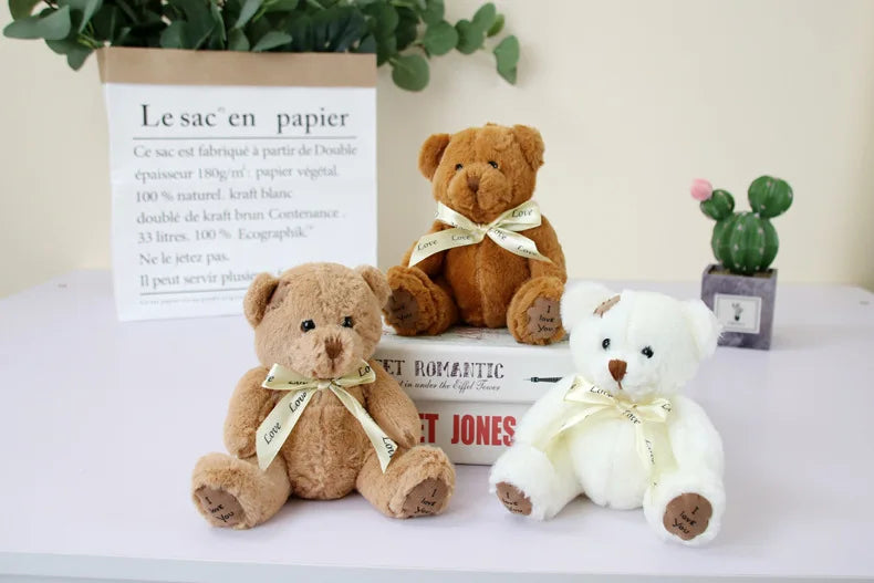 A set of three adorable teddy bear plush toys in various colors and sizes displayed next to a paper bag