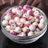 A bowl filled with small, round ceramic beads in shades of white and pink floral patterns for jewelry making