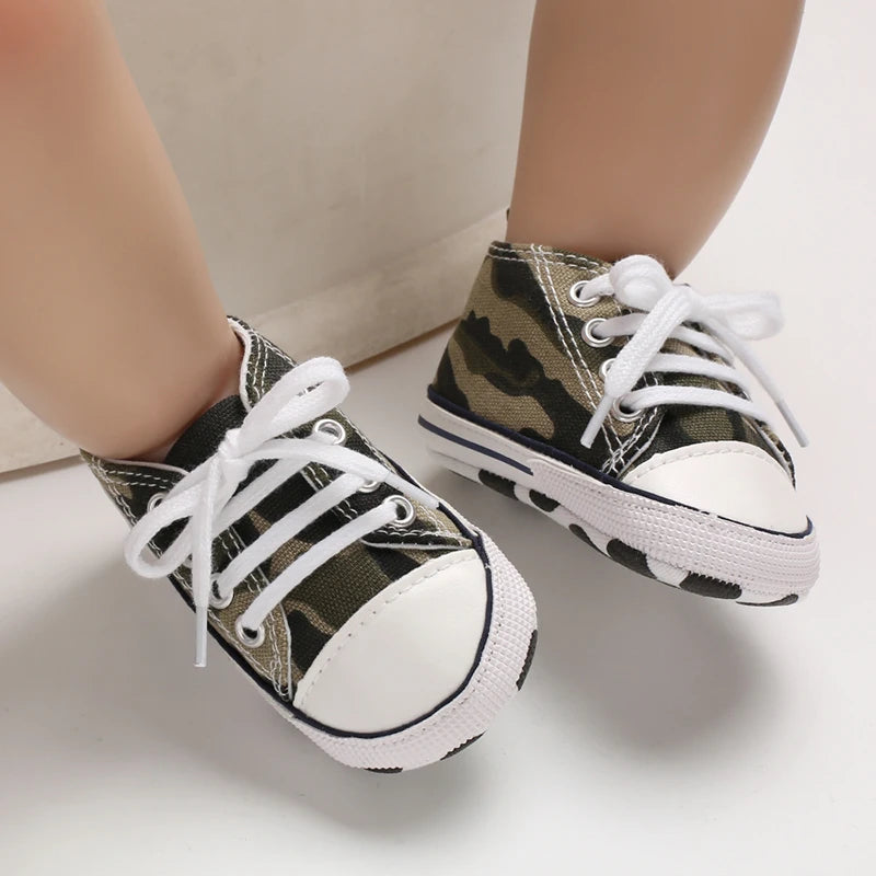 A pair of classic canvas first walkers for infants featuring a camouflage pattern and white laces.