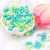 Assorted pearl beads in shades of blue and green are displayed next to a pink flower.
