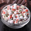 A clear glass bowl filled with small white ceramic beads decorated with red and green floral patterns.