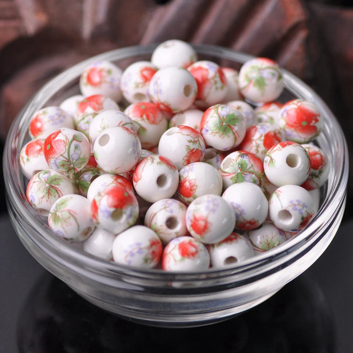 A clear glass bowl filled with small white ceramic beads decorated with red and green floral patterns.