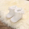 Pair of white plush baby snow boots with fluffy trim resting on a light beige faux fur rug.