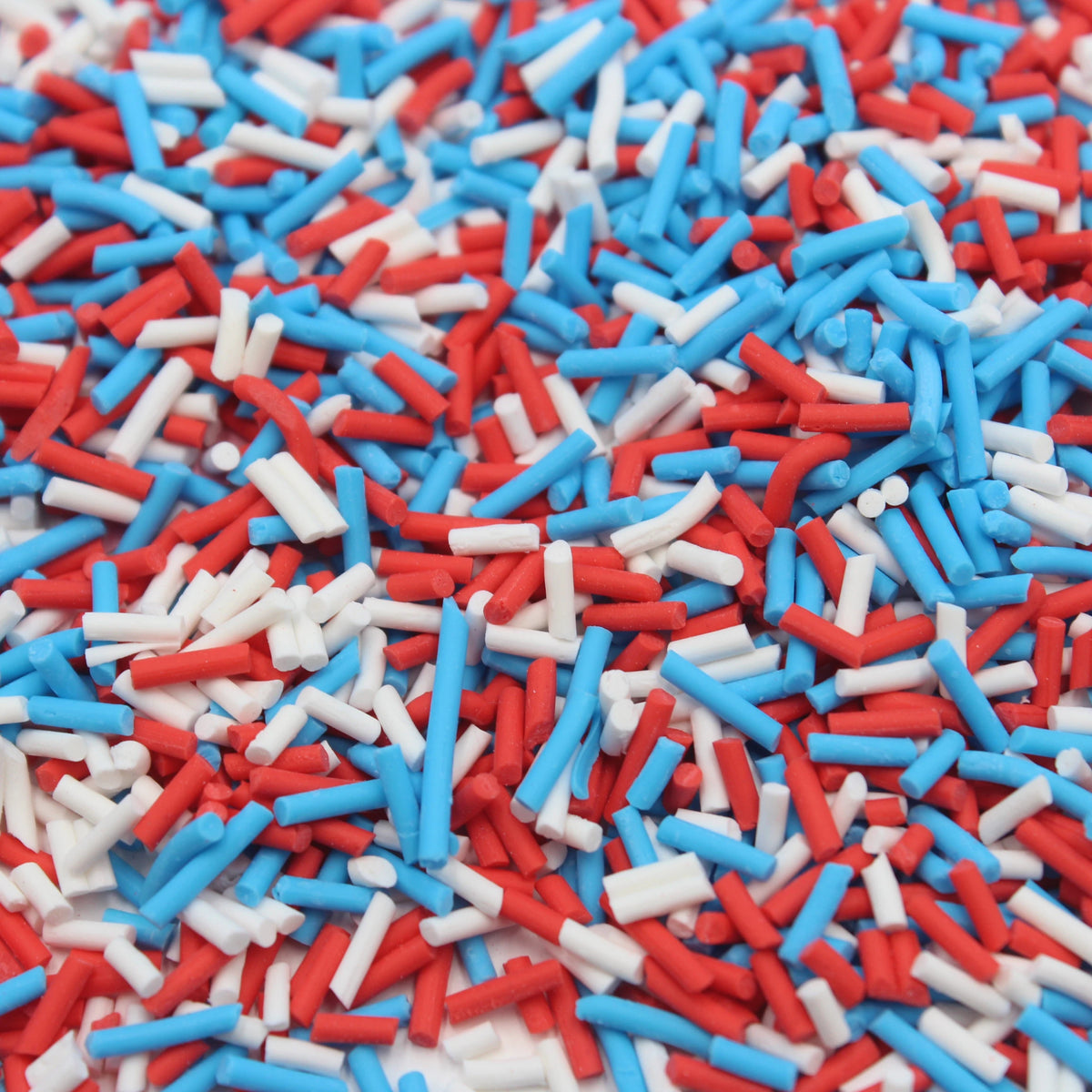 A close-up view of red, white, and blue soft polymer clay candy sprinkles scattered on a surface.