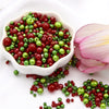 A bowl filled with a mix of red and green pearl beads for jewelry making, with loose beads scattered nearby.