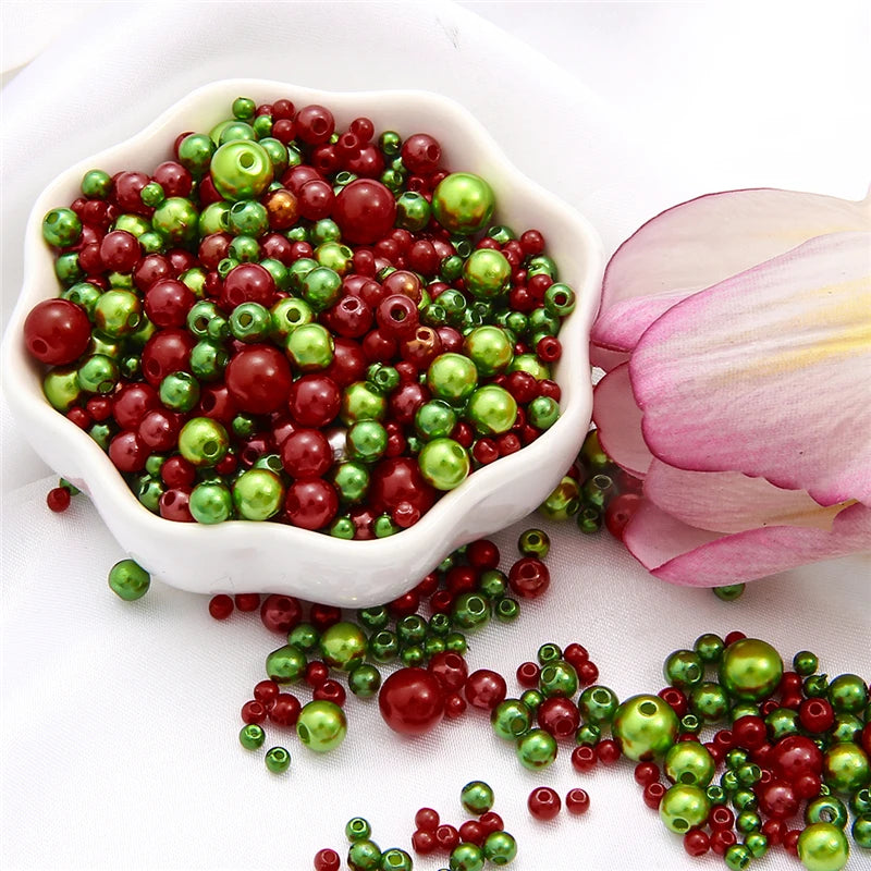 A bowl filled with a mix of red and green pearl beads for jewelry making, with loose beads scattered nearby.