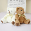 Two soft teddy bear plush toys, one white and one brown, lying on a white surface.