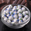 A clear glass bowl filled with small white and blue floral ceramic beads for jewelry making