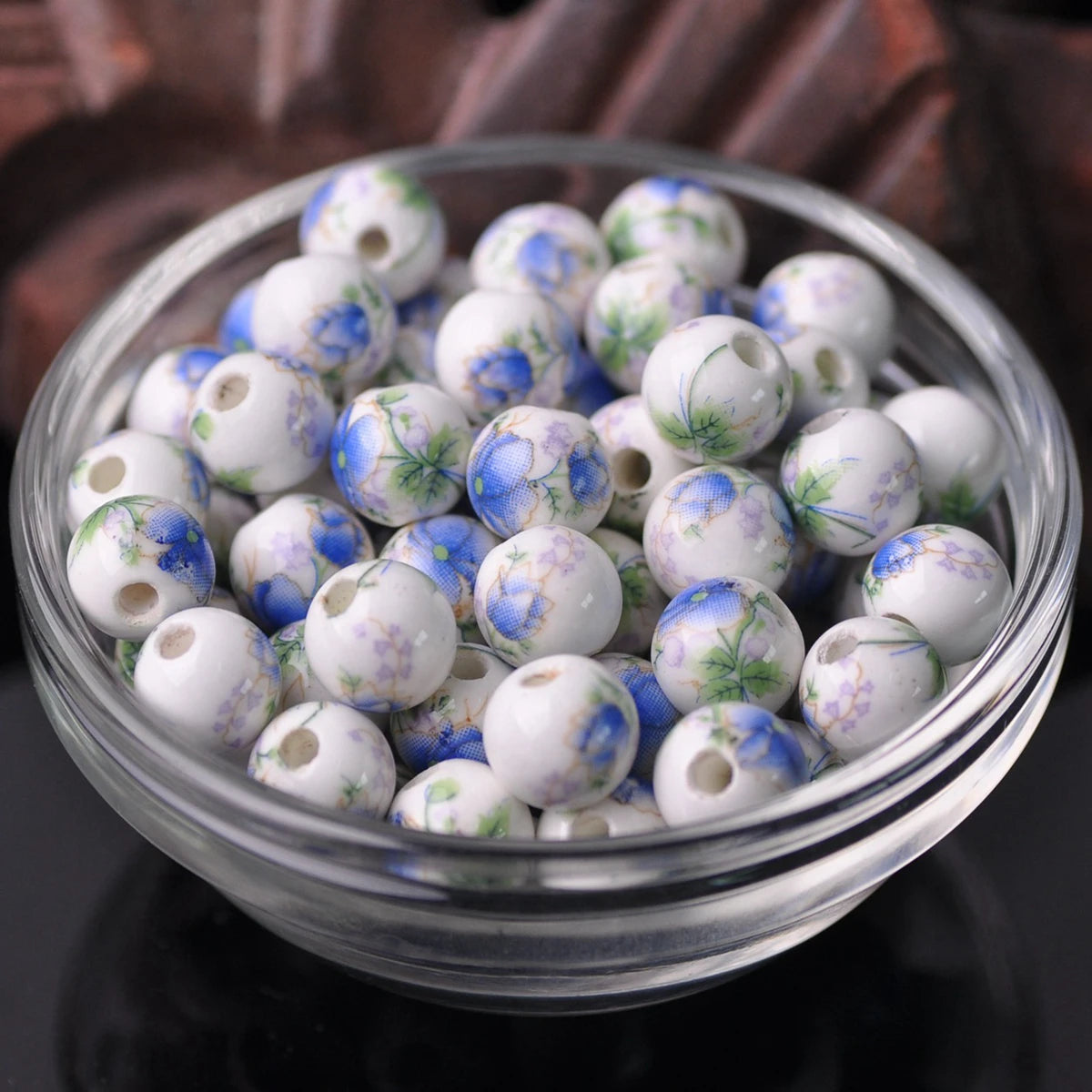 A clear glass bowl filled with small white and blue floral ceramic beads for jewelry making