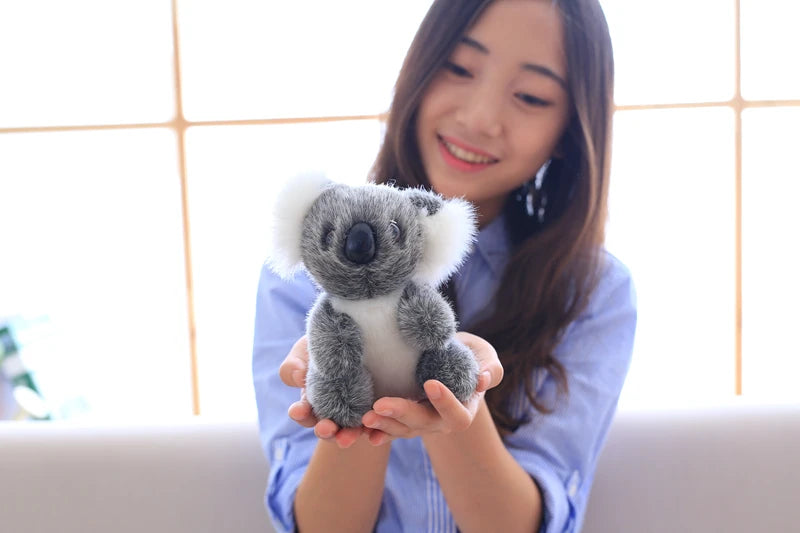 A young woman is holding a gray koala plush toy with white fur against a bright window background.