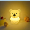 A glowing yellow koala night light sits on a surface next to a small wooden box and a spherical object.