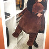 An oversized lifelike brown bear plush cushion is being held by a person in a white shelving unit.