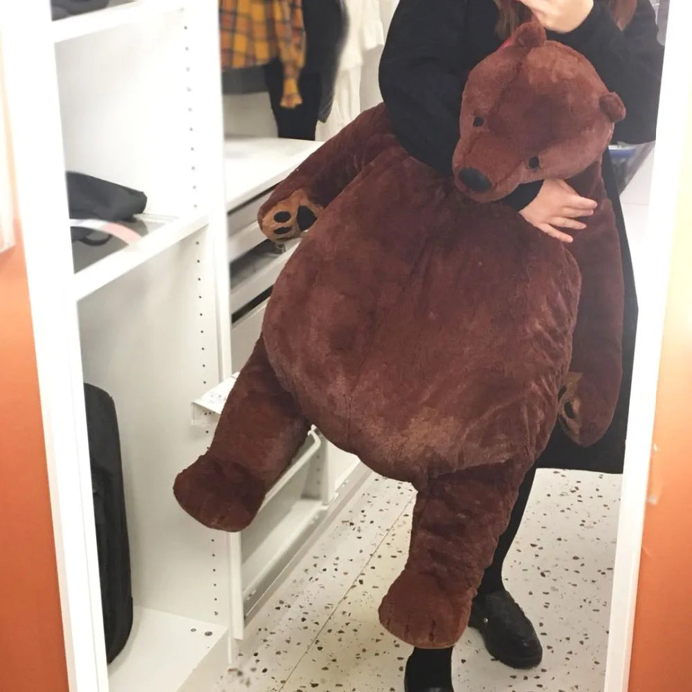 An oversized lifelike brown bear plush cushion is being held by a person in a white shelving unit.