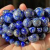 A handful of natural gemstone beads in various shades of blue and gray are held in a person's hand.