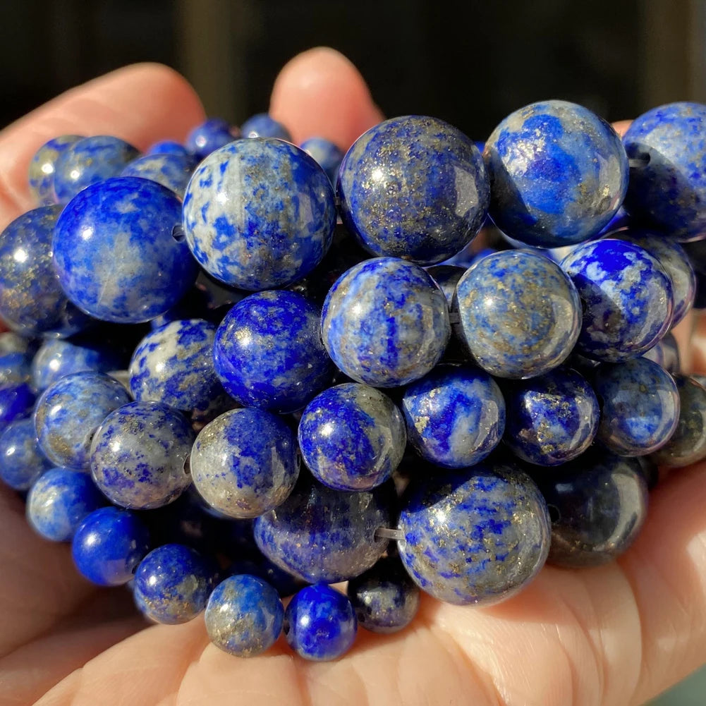 A handful of natural gemstone beads in various shades of blue and gray are held in a person's hand.