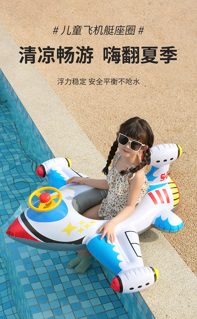 A child is sitting in a white and blue inflatable aircraft swim ring on a tiled poolside.