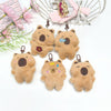 Several small, fluffy brown capybara plush keychains are displayed with a pink mesh bag in the background.