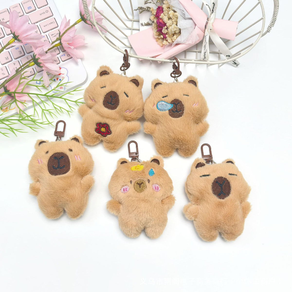 Several small, fluffy brown capybara plush keychains are displayed with a pink mesh bag in the background.