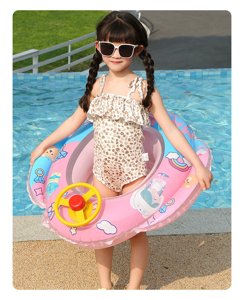 A young girl is sitting in a pink inflatable aircraft swim ring with a yellow steering wheel in blue water.