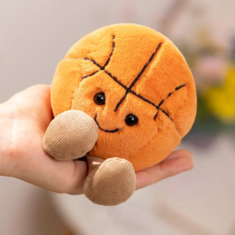 An orange plush sports ball companion with stitched lines and small feet is held in a hand.