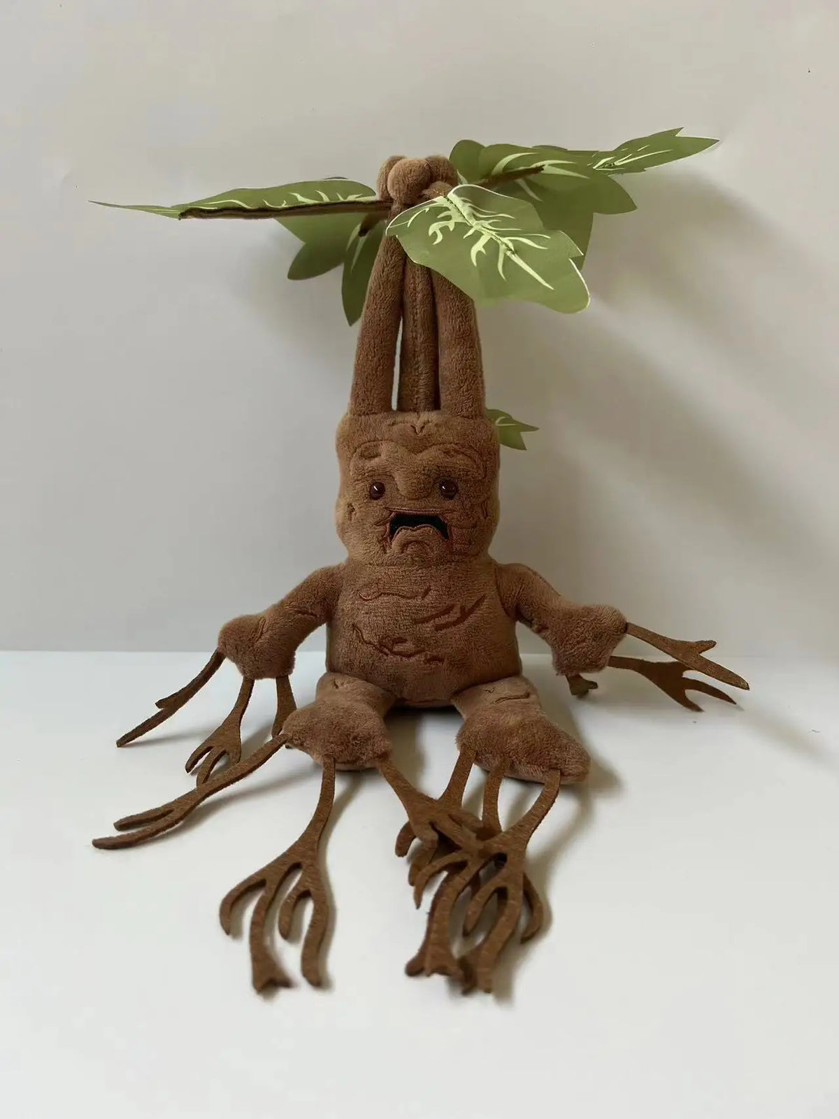 A brown mandrake plush toy with large leaves, standing on a white surface.