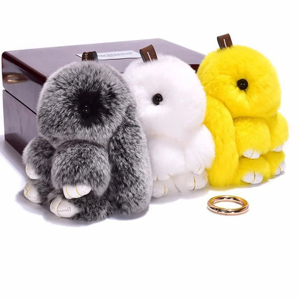 Three plush bunny keychains in gray, white, and yellow are displayed next to a dark box.
