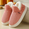 A pair of pink knitted slippers with white faux fur lining resting on a light surface.