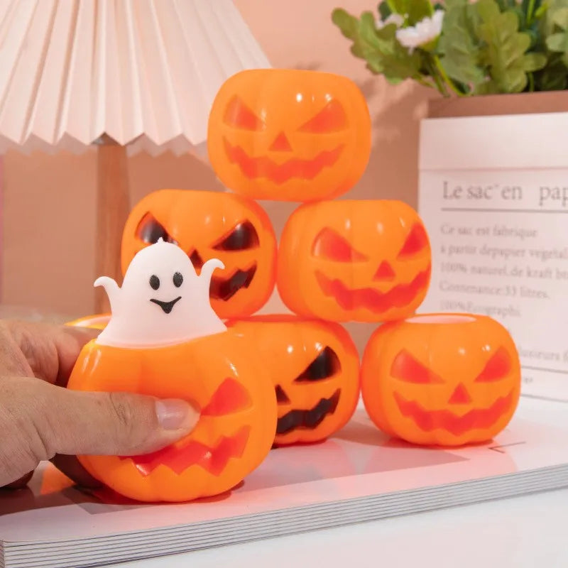 A hand holds an orange pumpkin shaped squishy ghost fidget toy next to several other similar orange pumpkin toys.