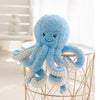 A fluffy blue octopus plush toy with hanging loops displayed on a gold wire stand.