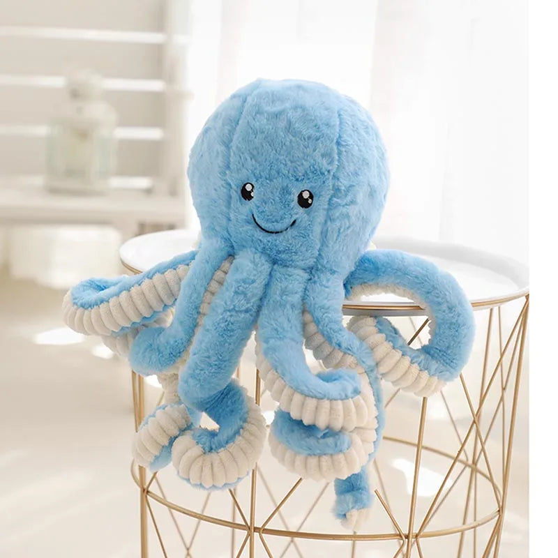 A fluffy blue octopus plush toy with hanging loops displayed on a gold wire stand.