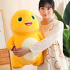 A woman is holding a yellow dinosaur plush toy with a smiling face.