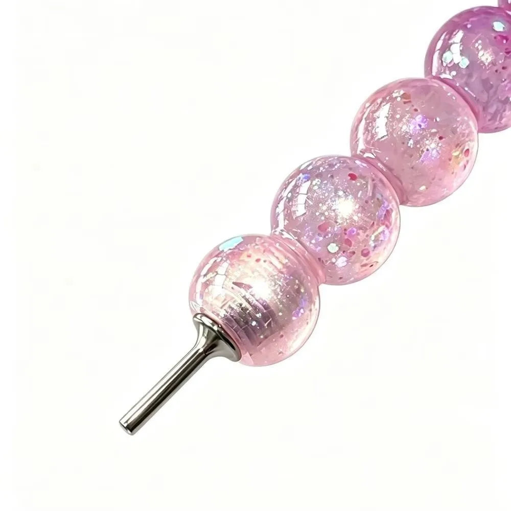 A series of pink glitter balls attached to a metal pen tip for diamond painting.