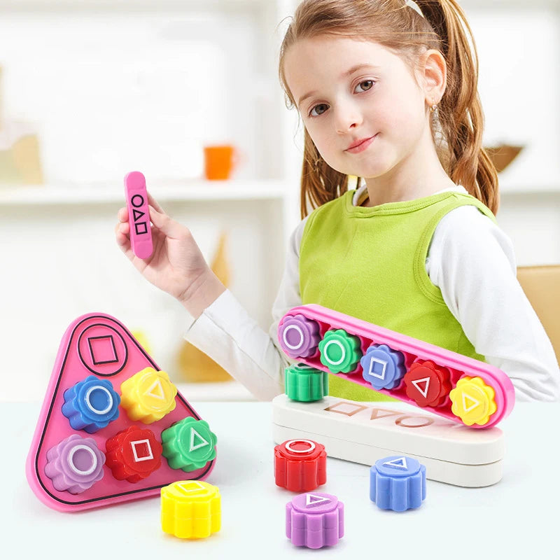 A young girl holds a pink gonggi stone and various colored stones on a white table.
