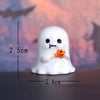 A white ghost-shaped figurine with black eyes and an orange flower accessory, shown against a blurred sunset background.