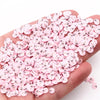 A hand holds a large pile of pink polymer clay slices for DIY crafts.