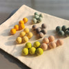 A collection of colorful, smooth, egg-shaped sensory balls in shades of yellow, green, and gray arranged on a white cloth.
