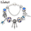 Silver crystal charm bracelet featuring blue stones and green leaf floral accents.